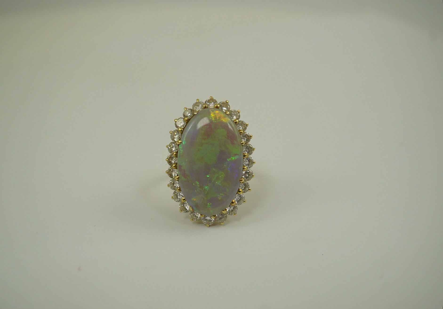 An 18ct gold, white opal and diamond set oval cluster dress ring, the cabochon opal measuring approximately 22mm by 14.5mm, with a depth of 5mm, and bordered by round brilliant cut diamonds, size L, gross weight 6.8 gram